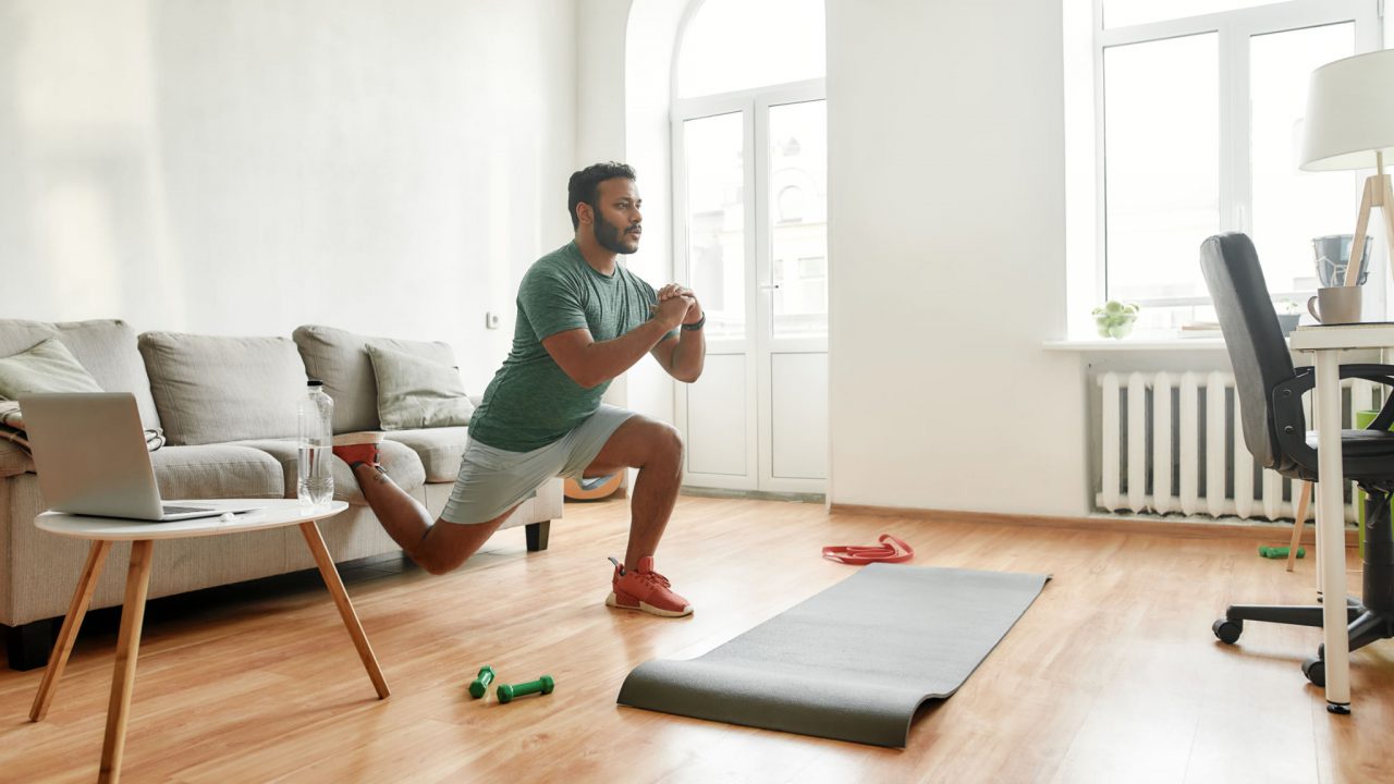 young active man watching online video training on laptop and performing a deep bulgarian split-squat